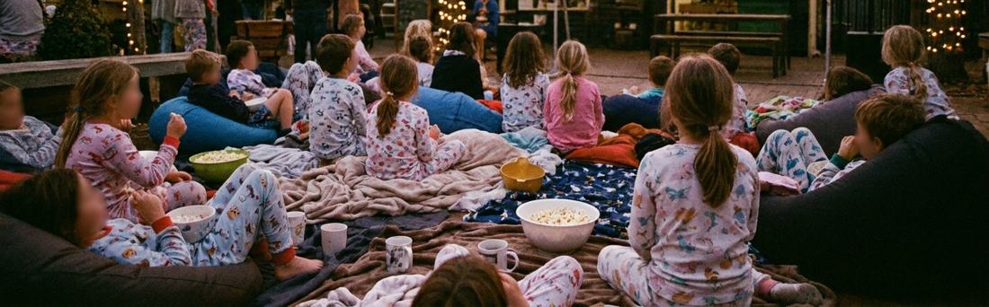 Kids in pyjamas watching a movie under fairy lights
